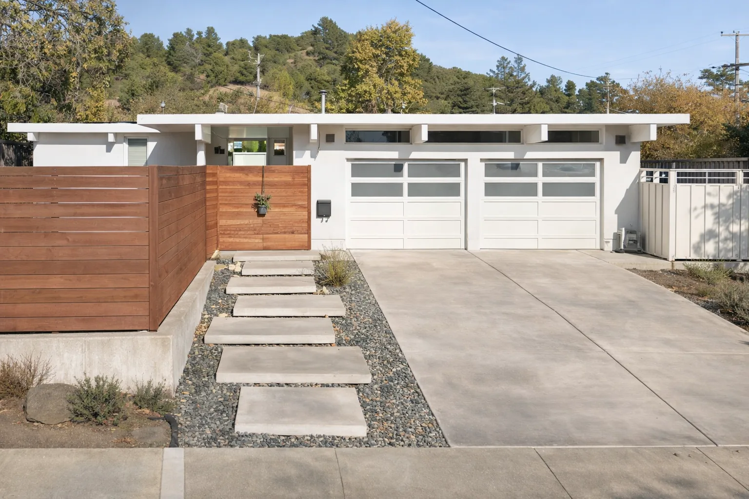 AI-generated illustration of a white Eichler with a flat roof, clerestory windows over a double garage, and a horizontal redwood entry fence, with a wooded ridge behind.