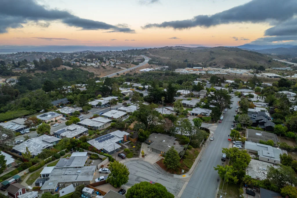 An aerial at dusk over the Highlands showing mostly single-storey flat-roofed Eichlers, with several larger two-storey houses visible among them.