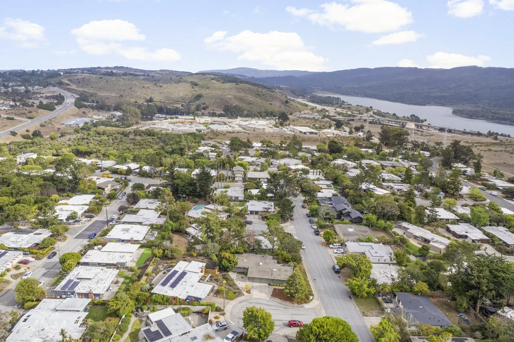 A daylight aerial over the San Mateo Highlands: hundreds of low flat-roofed Eichlers on curving streets, running up to Crystal Springs Reservoir and the undeveloped watershed hills.