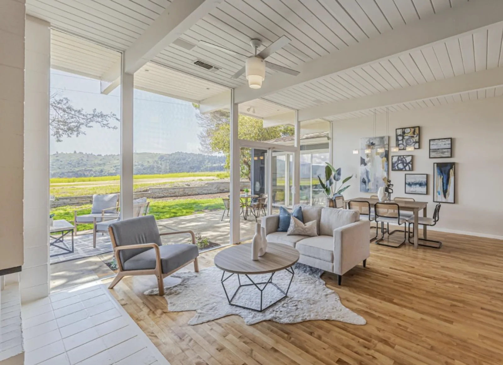 A living and dining space with a glazed corner, exposed beams overhead and a sliding wall open to the patio and meadow.