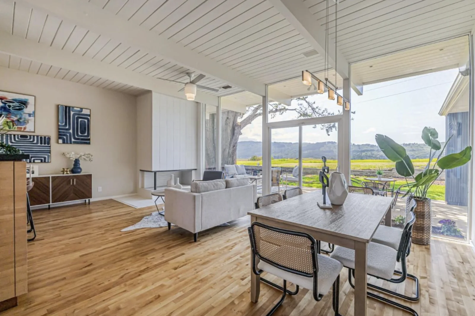 A wide view from the kitchen counter across the living room to the dining area, with the beamed ceiling running the full length and glass on two sides.