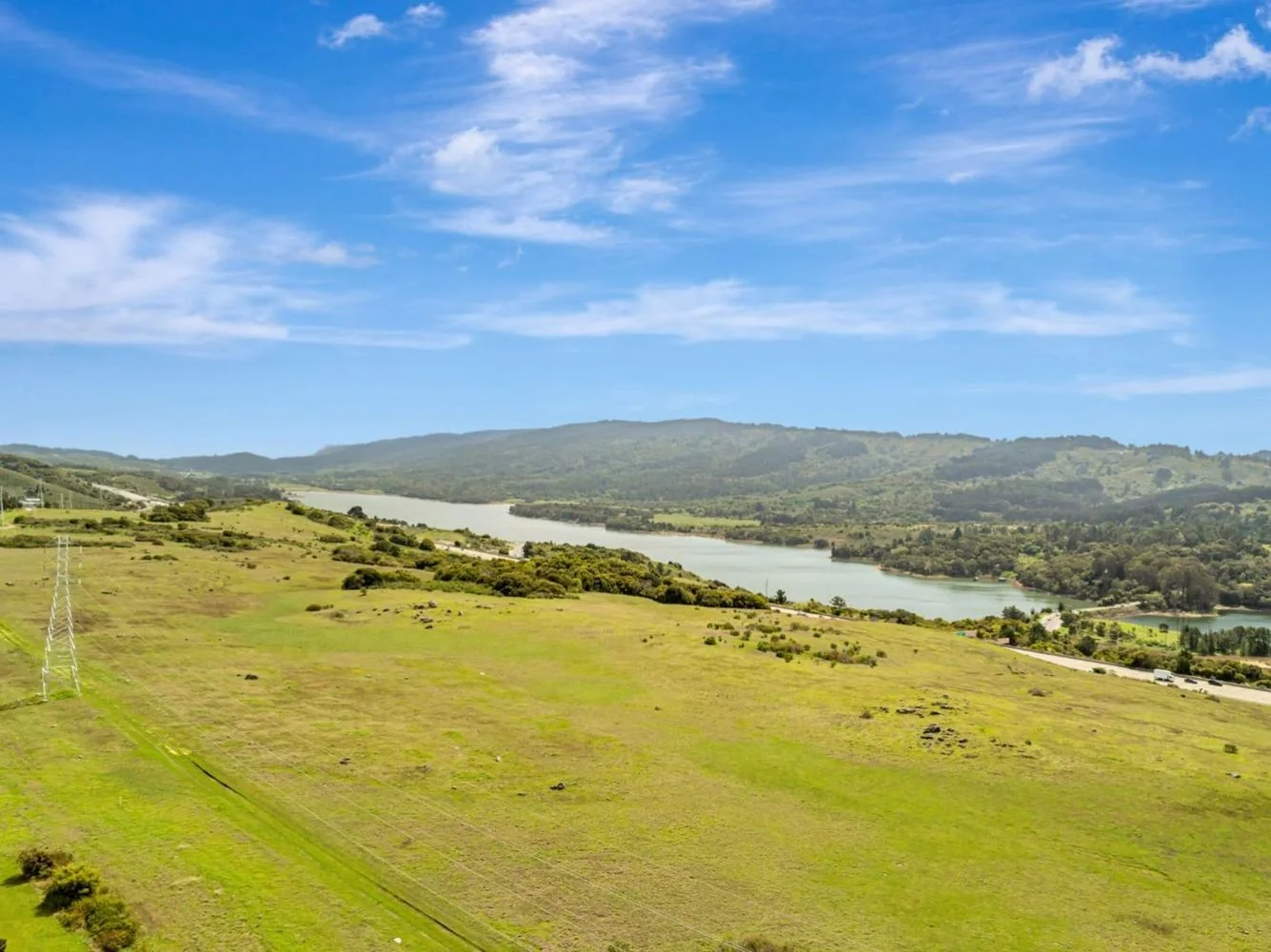 Looking west from the edge of the tract across open green grassland to Crystal Springs Reservoir and the long wooded ridge of the Peninsula watershed beyond.