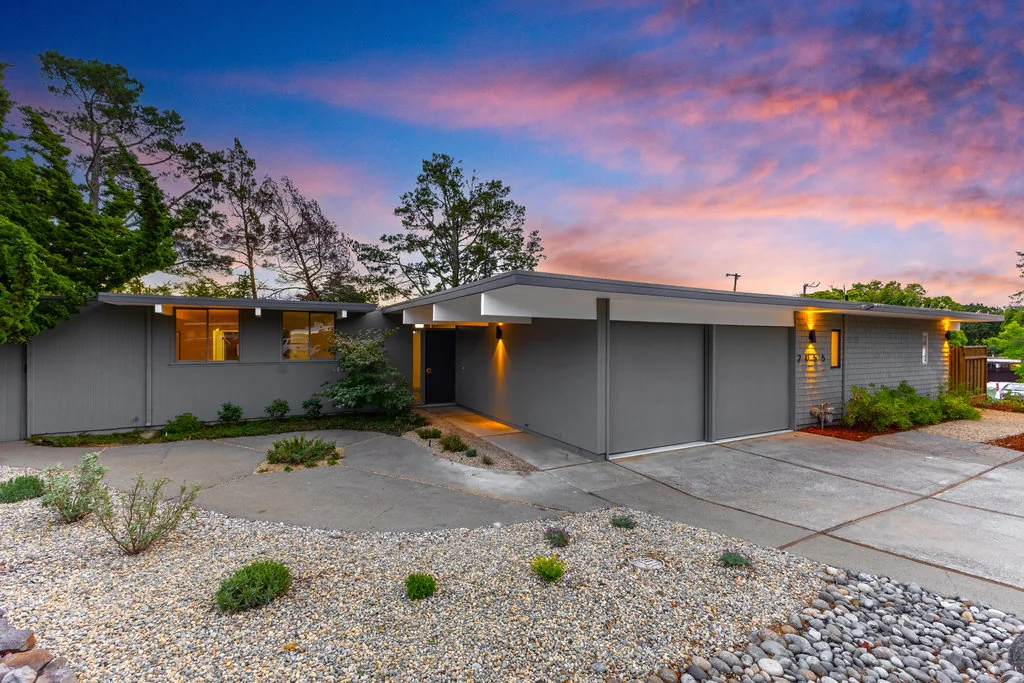 The entry court of a San Mateo Highlands Eichler at dusk, glazed on both sides and open to the sky, lit from within.