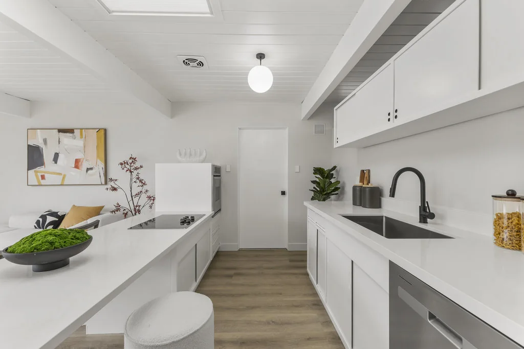 A galley kitchen with white counters and cabinets, a skylight overhead, and a counter running out to become a breakfast bar.