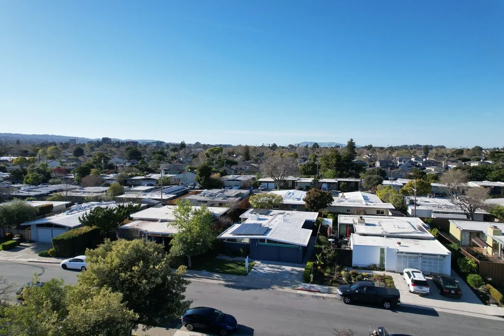 An oblique aerial over 19th Avenue Park: block after block of low flat-roofed Eichler homes on a flat bay plain, with hills in the far distance.